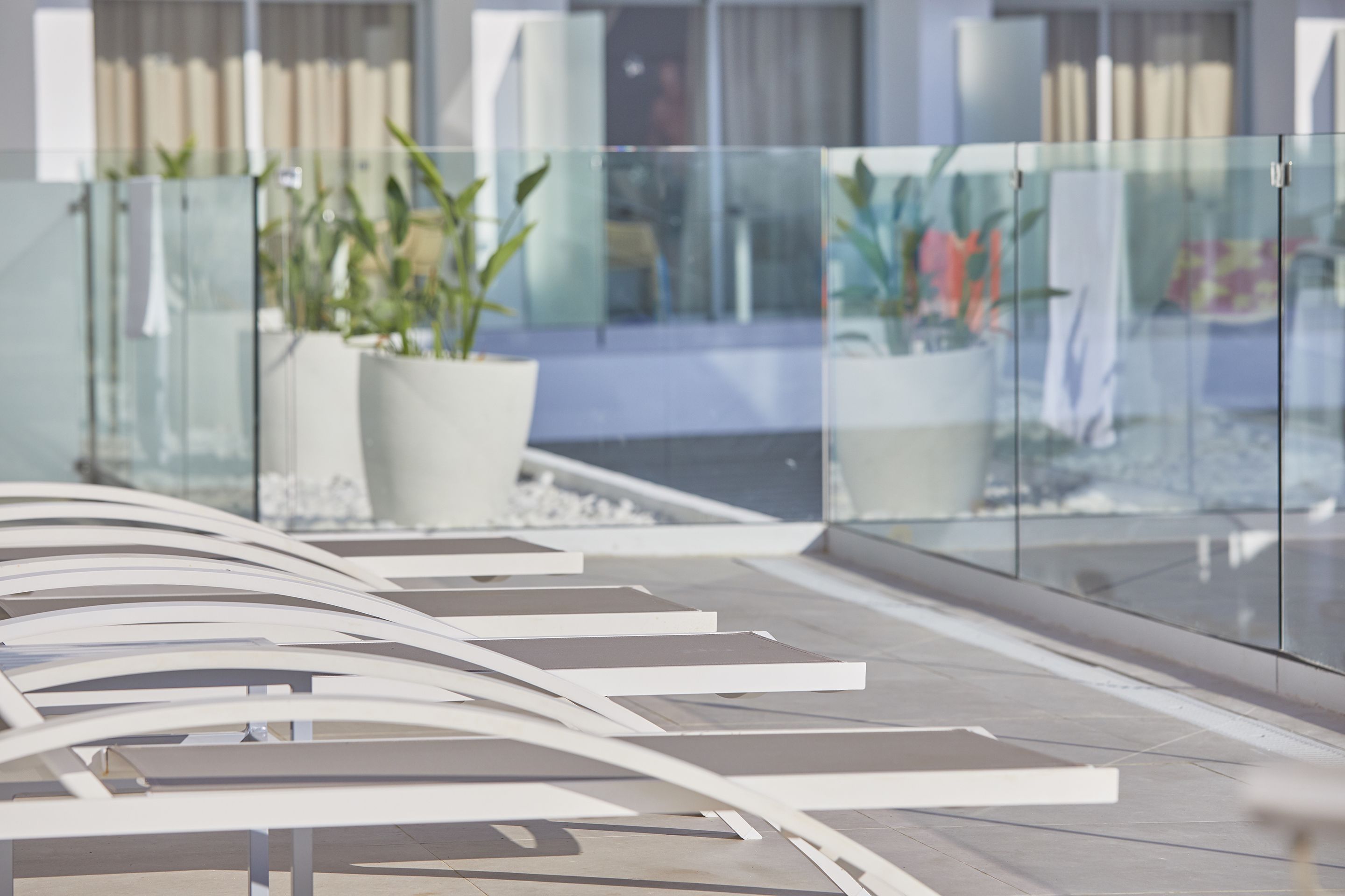 A modern indoor space with glass railings, potted plants, and a tiled floor.