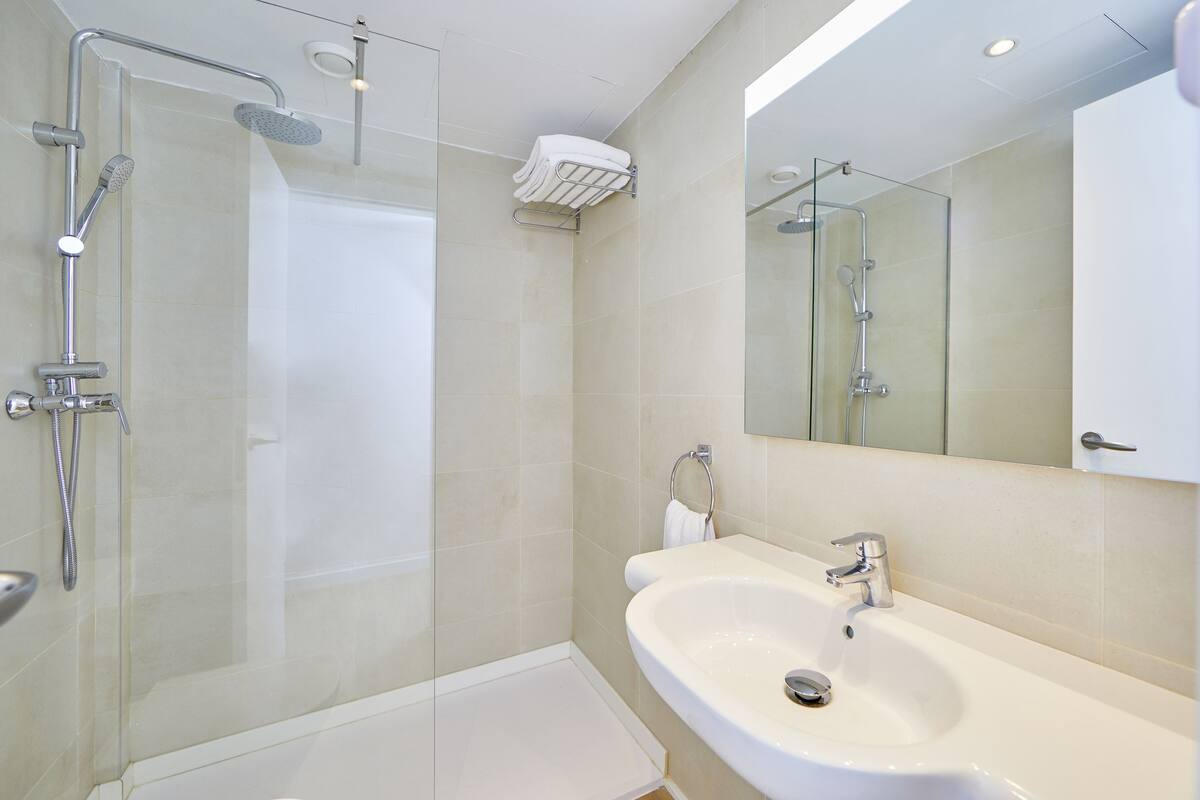 A modern bathroom with a glass-enclosed shower, a white sink, and a large mirror.