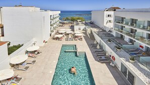 Un área de piscina con una persona nadando, sillas de descanso y sombrillas.