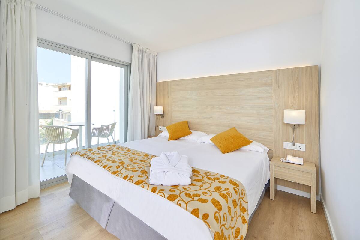 A hotel room with a large bed, two bedside lamps, a wooden headboard, and a view of the outside.