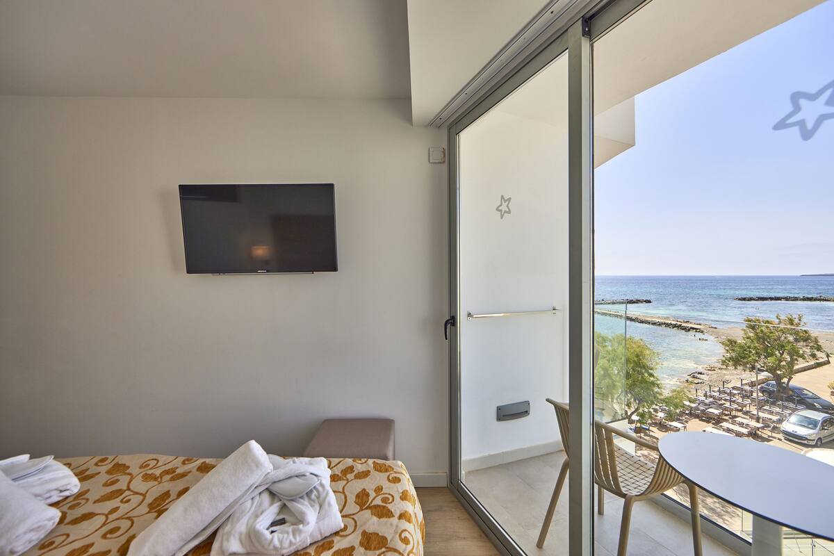 A hotel room with a bed, a TV, a balcony with a view of the beach and ocean.