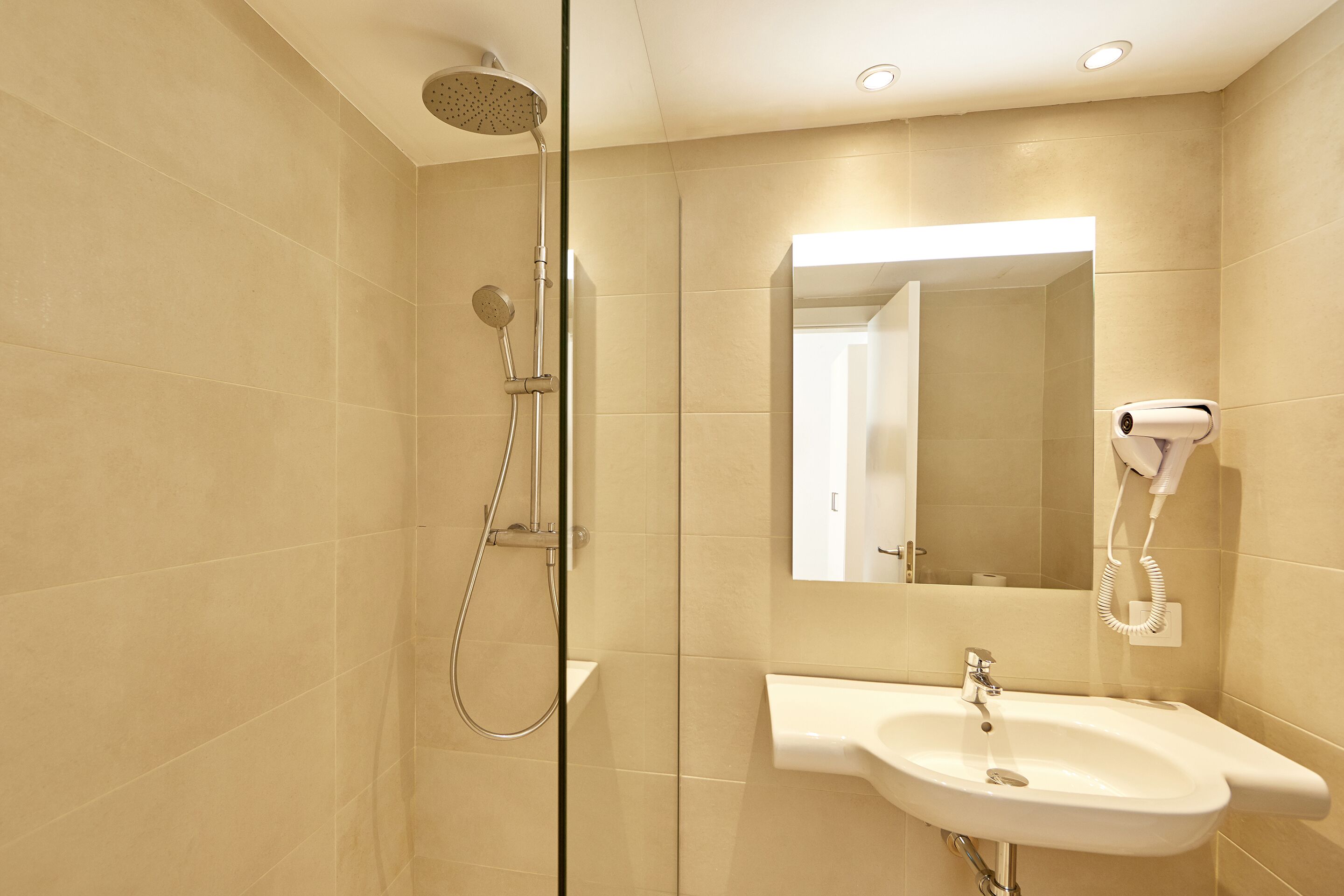Un baño moderno con cabina de ducha de vidrio, un lavabo blanco y un secador de pelo montado en la pared.