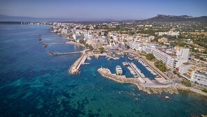 Vista aérea de una ciudad costera con un puerto deportivo, edificios y una colina con una fortaleza.
