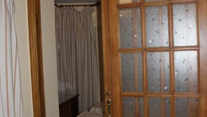 A room with a wooden door with glass panels, a bed with a striped bedspread, and a curtain on the left. - Hostal Andalucía (Almunecar)