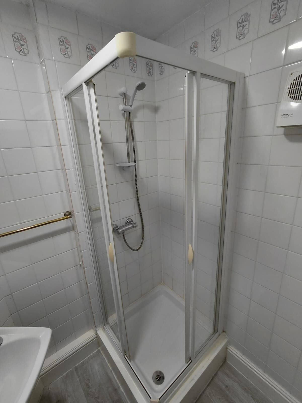 Une cabine de douche fermée par des parois en verre, dotée d’un pommeau de douche à main et d’un robinet mural.