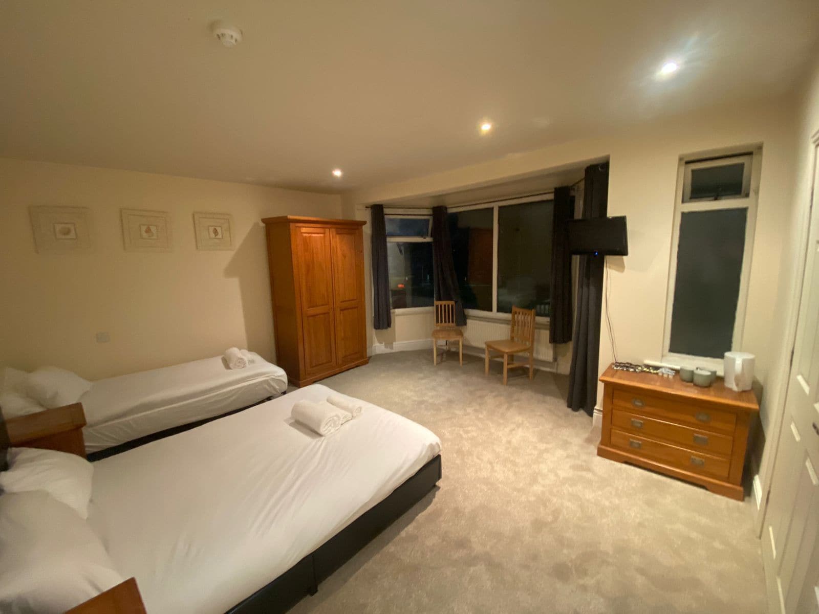 Quarto com duas camas, guarda-roupa de madeira, escrivaninha com cadeira e janela com vista.