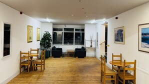 A spacious room with wooden flooring, a large window, and several chairs arranged for seating. - Sea Side Hotel (Skegness)