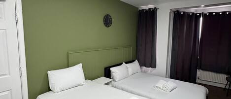 A hotel room with two beds, green walls, a clock, and a window with curtains.