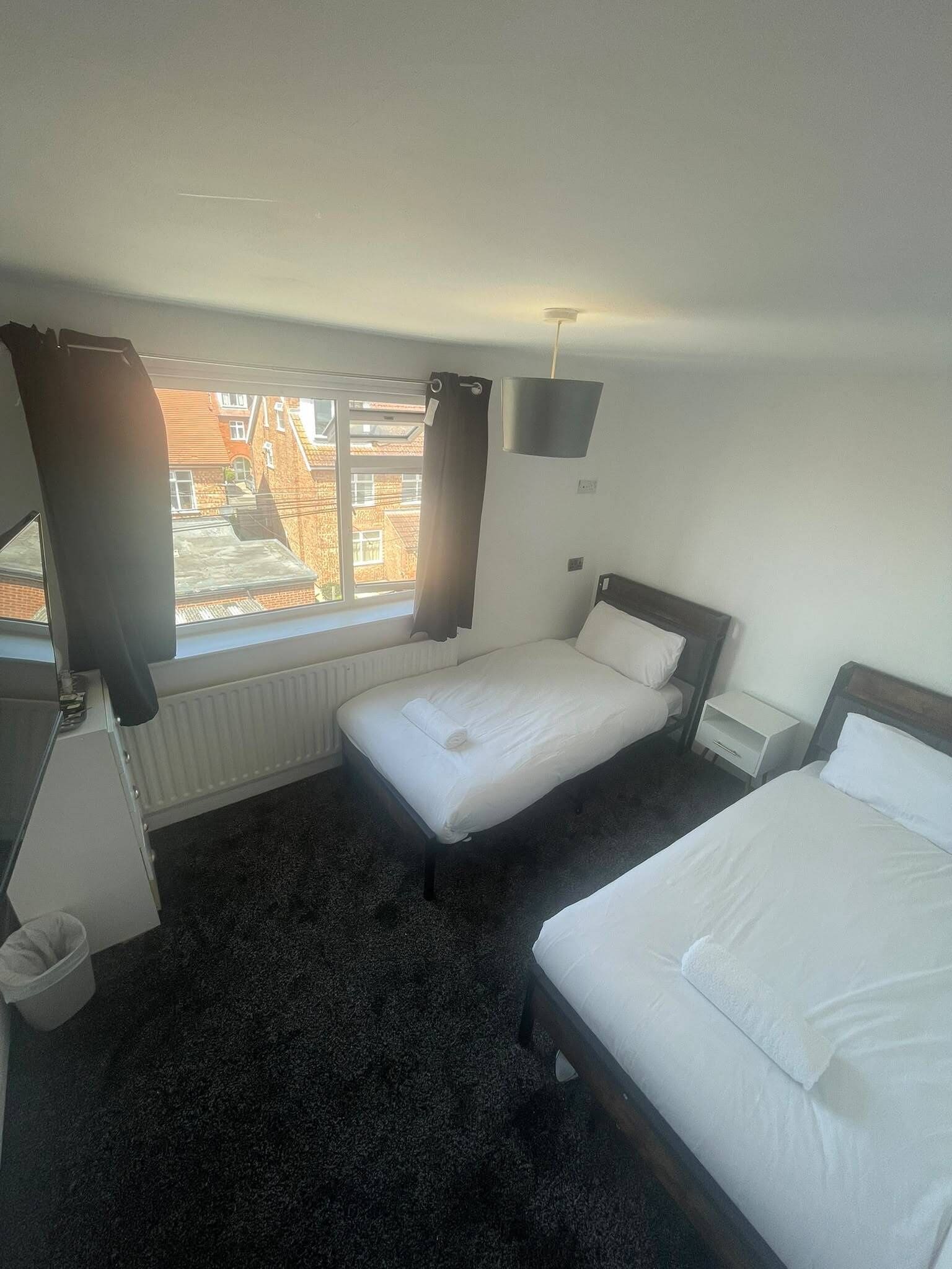 A hotel room with a bed, a bedside table, a window with curtains, and a radiator.