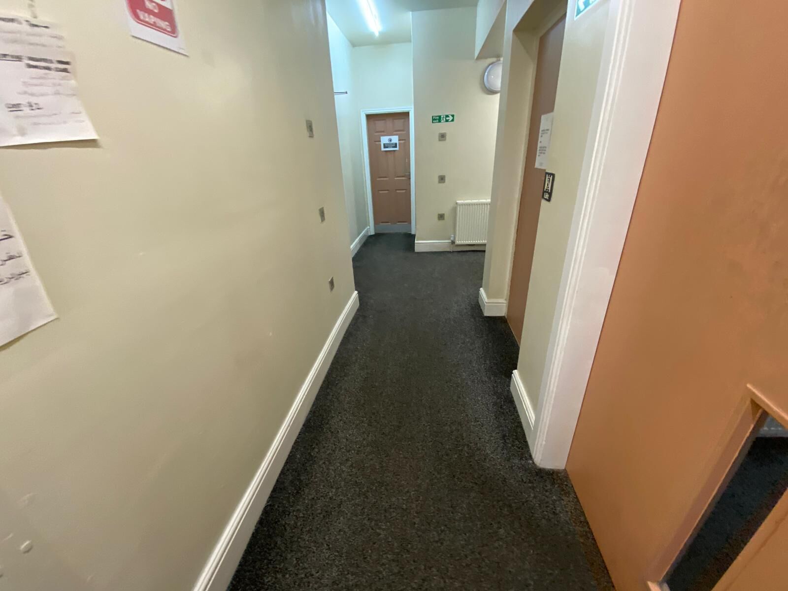 Un couloir aux murs de couleur beige, avec un tapis foncé et une porte au fond.