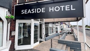 A sign for Seaside Hotel with a wooden deck, outdoor seating, and a view of the street. - Sea Side Hotel (Skegness)