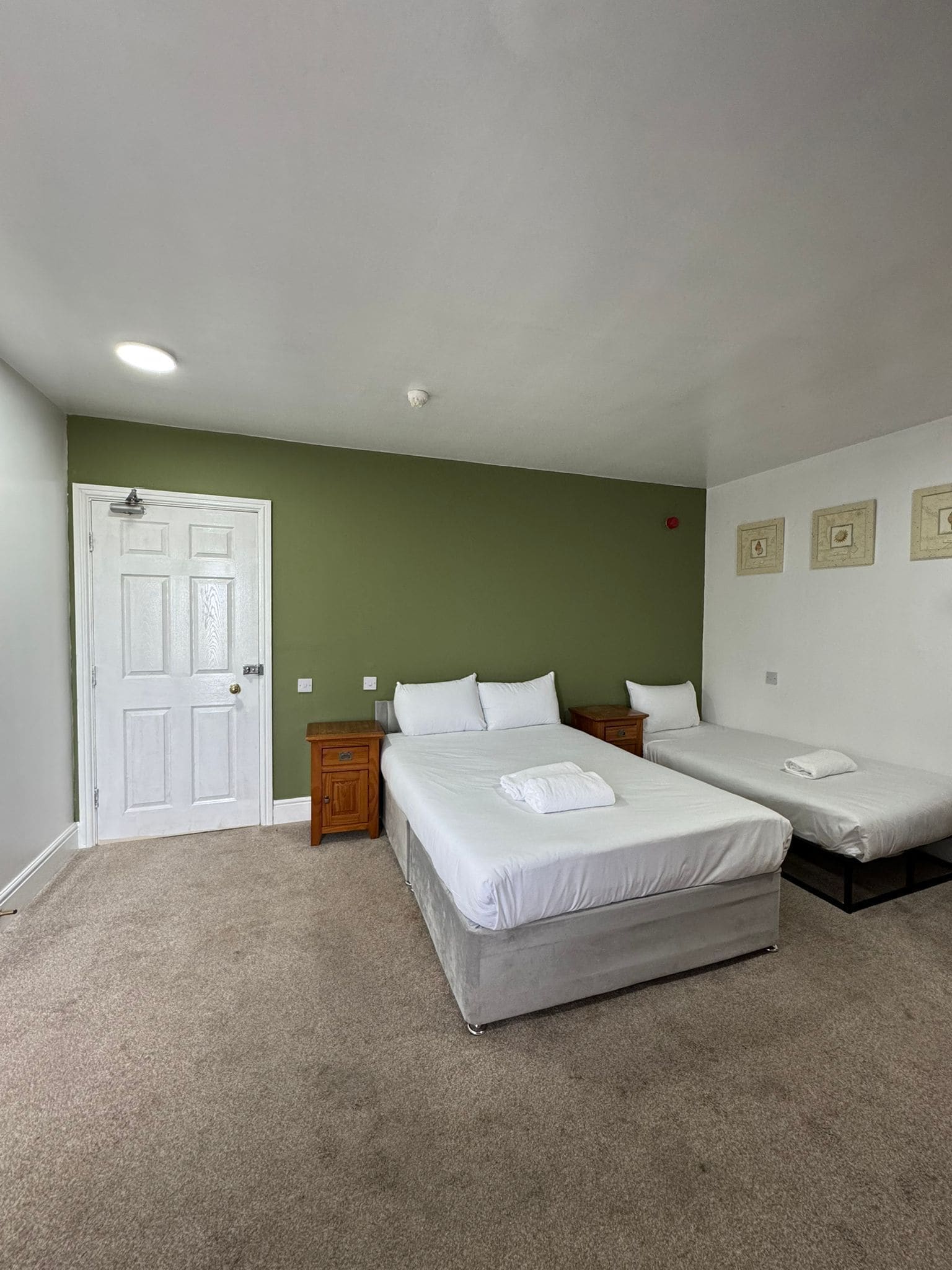 A room with two single beds, a door, and a small bedside table.