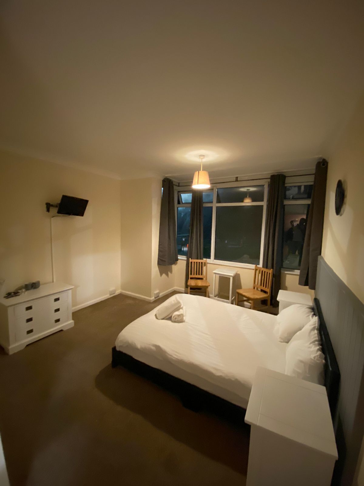 Ein Hotelzimmer mit einem großen Bett, einem Schreibtisch, einem Stuhl, einem an der Wand montierten Fernseher und einem Fenster mit Vorhängen.