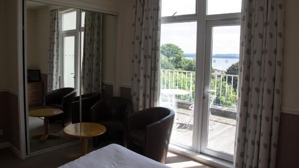 A hotel room with a balcony, a bed, two chairs, and a small table. - Sea Side Hotel (Skegness)