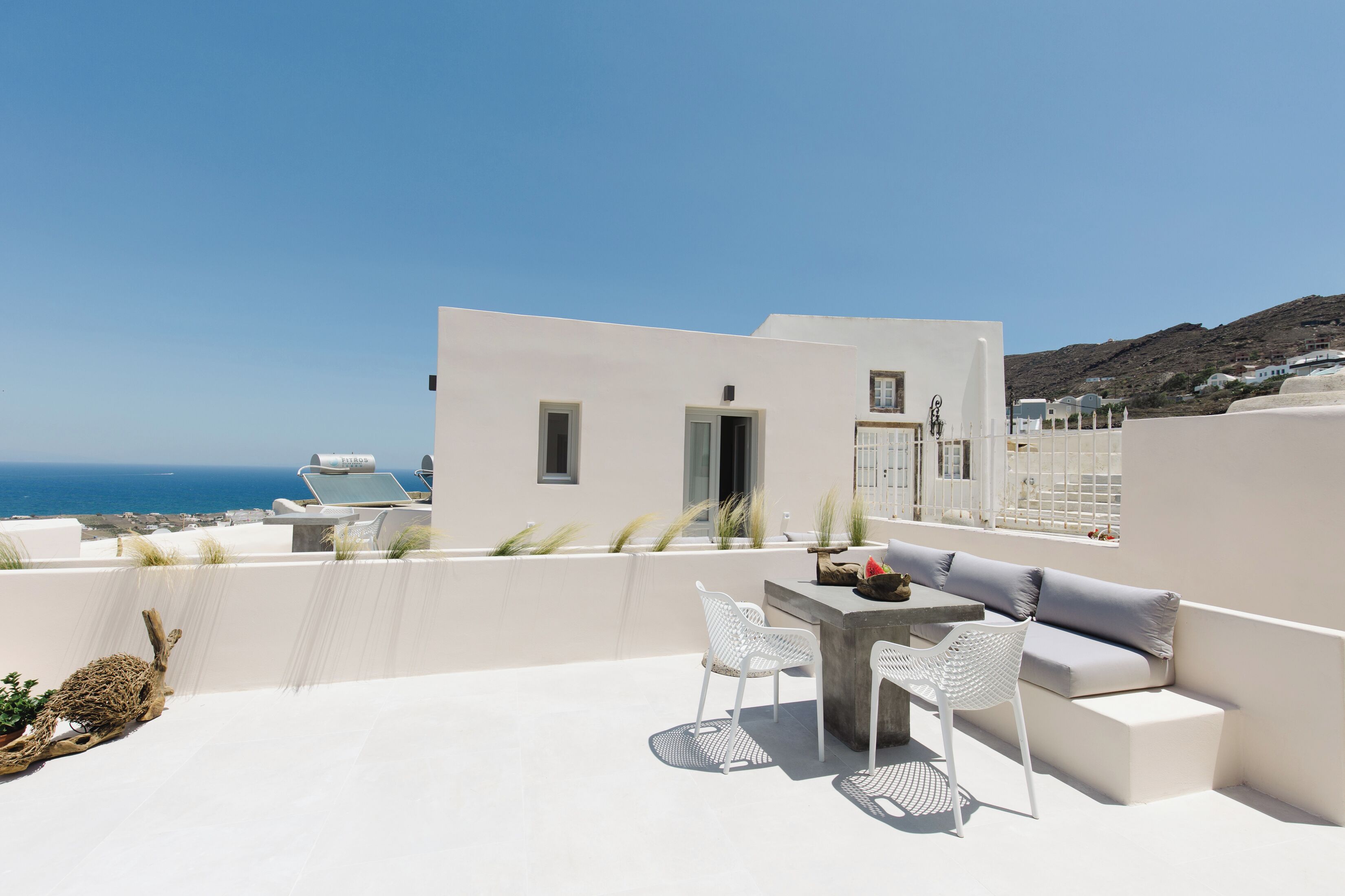 A rooftop terrace with a white building, a table with chairs, and a view of the sea.