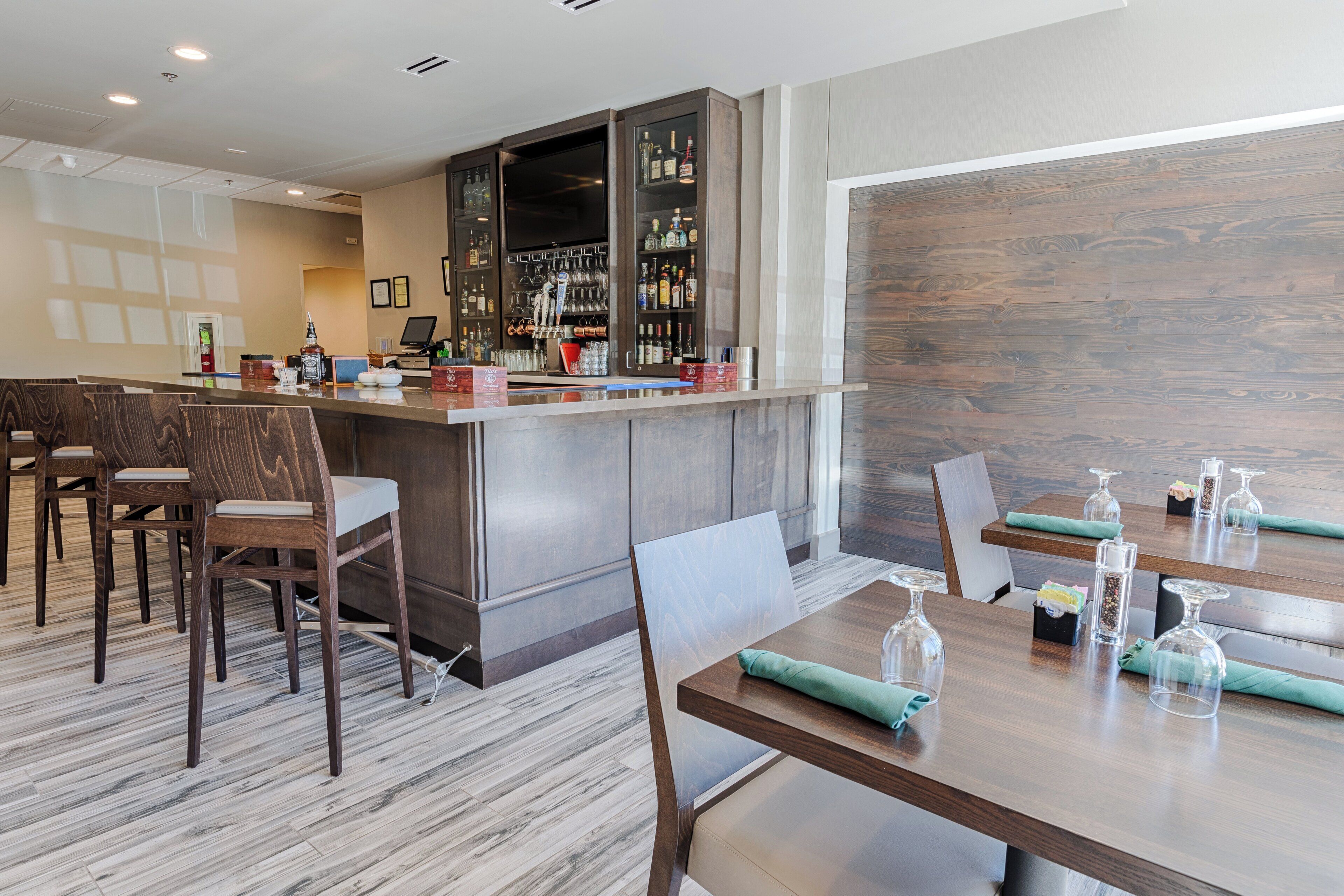 A bar area with a wooden counter, seating with cushioned chairs, and a variety of bottles and glasses on shelves.