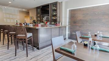 A bar area with a wooden counter, seating with cushioned chairs, and a variety of bottles and glasses on shelves.