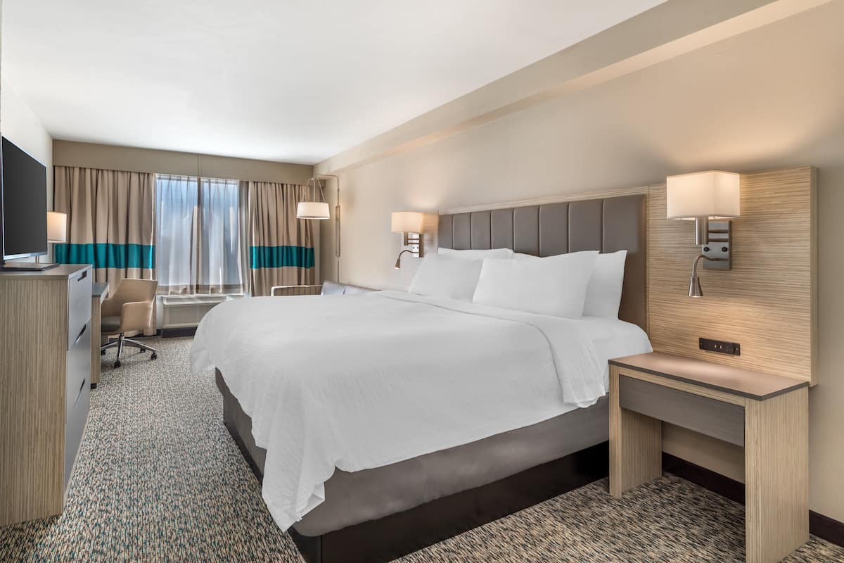 A hotel room with a large bed, a desk, a chair, and a television.