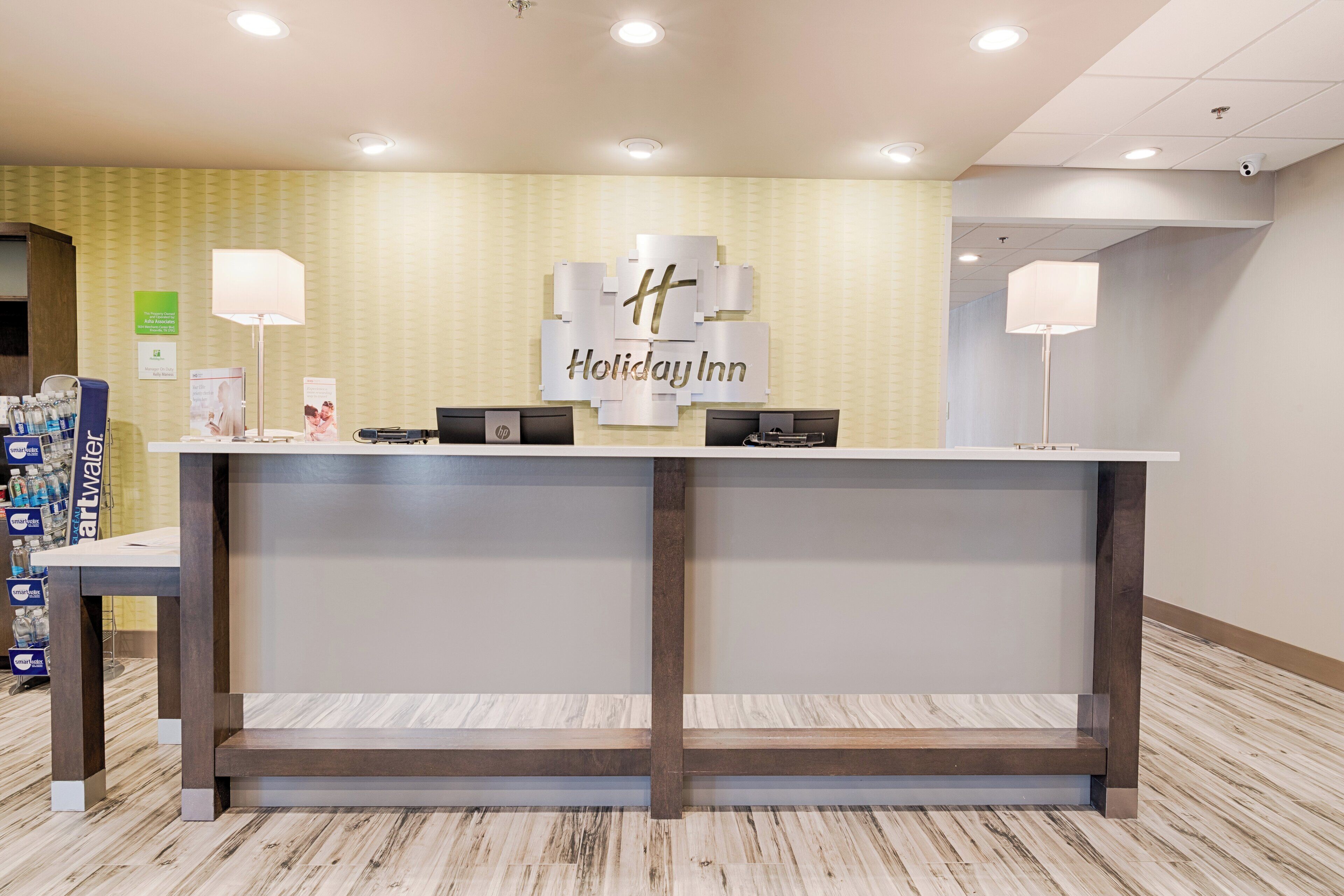 A reception desk with a Holiday Inn sign, two computer monitors, a telephone, and a water dispenser.
