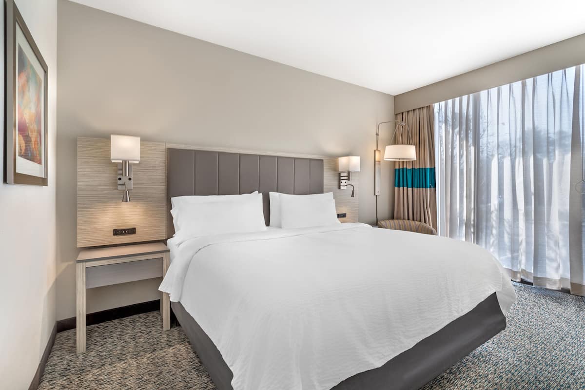 A hotel room with a large bed, bedside lamps, a nightstand, and a window with curtains.