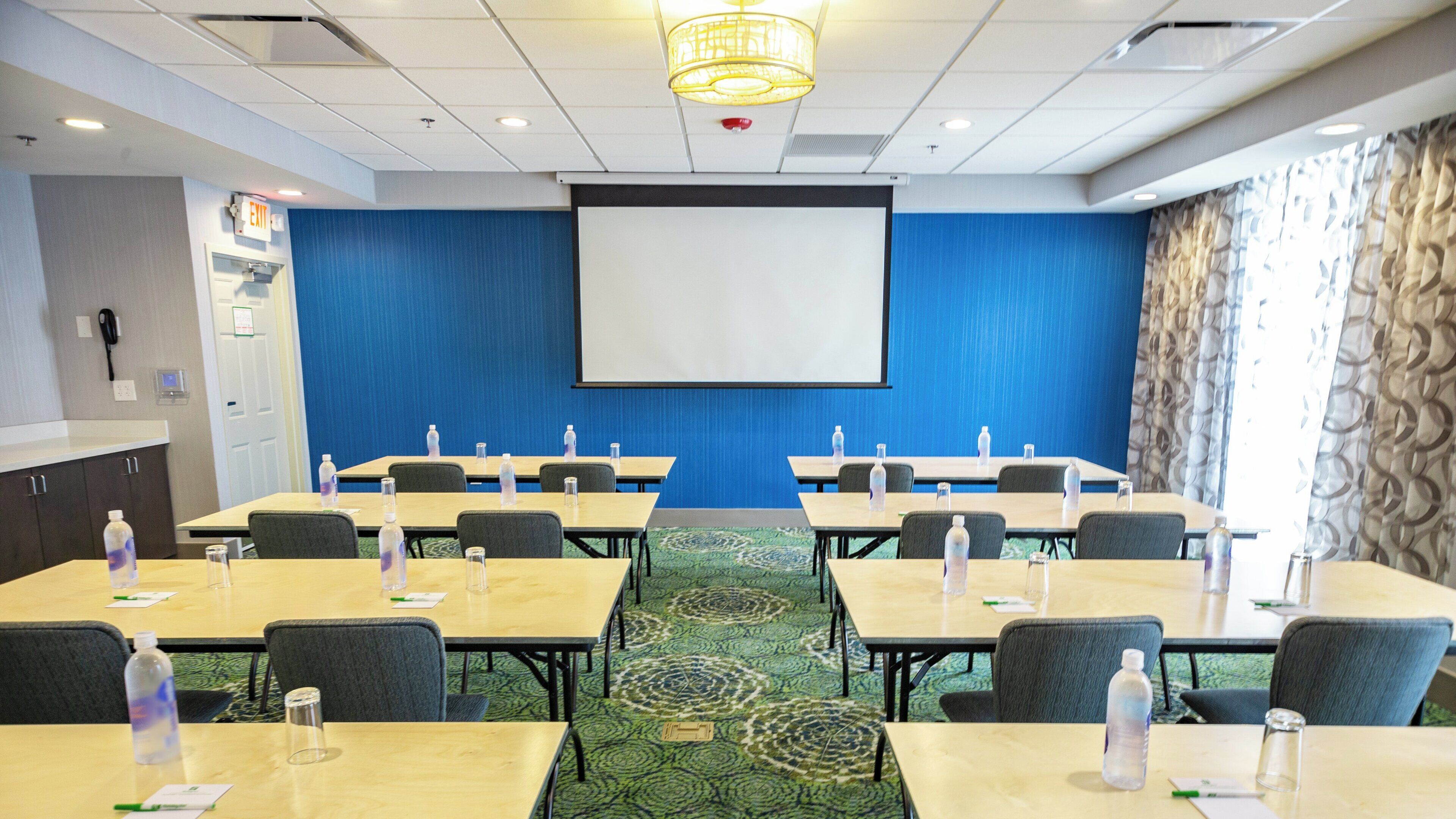 A conference room with a projector screen, tables, chairs, and a carpeted floor.