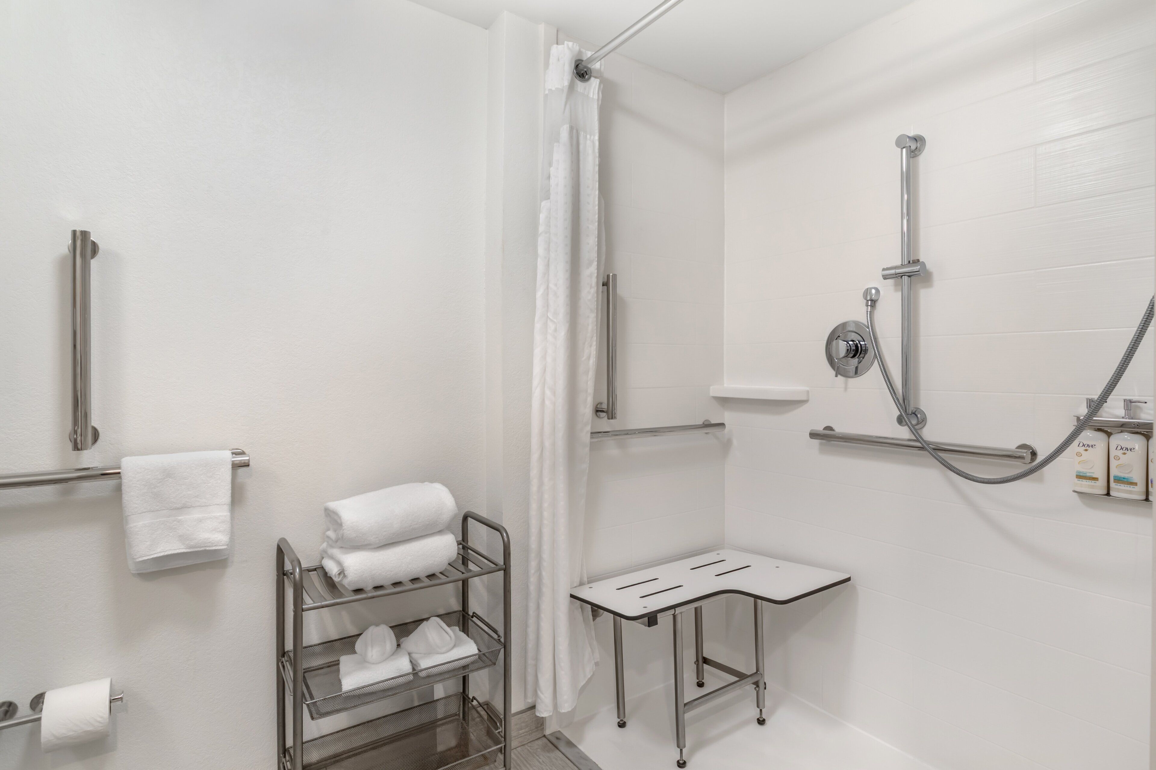 Un baño moderno con ducha, toallero, repisa con artículos de aseo y soporte para papel higiénico.