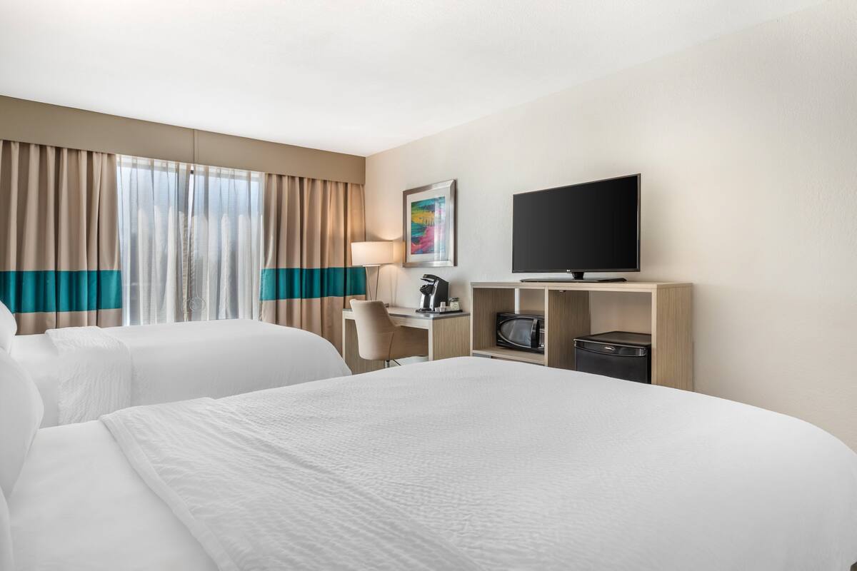 A hotel room with two beds, a desk, a television, and a window with curtains.