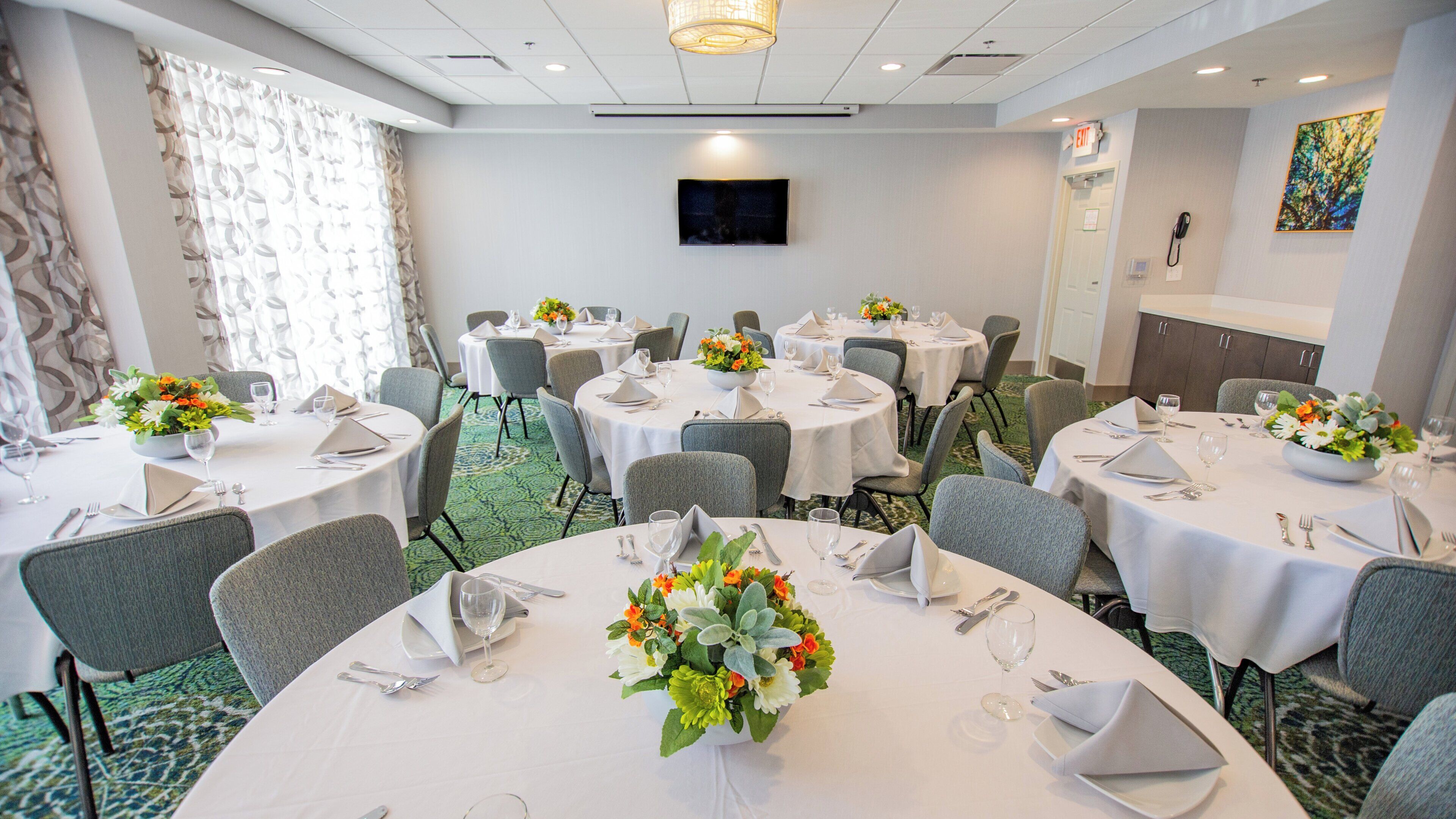 A hotel dining area with round tables, chairs, and flower centerpieces.