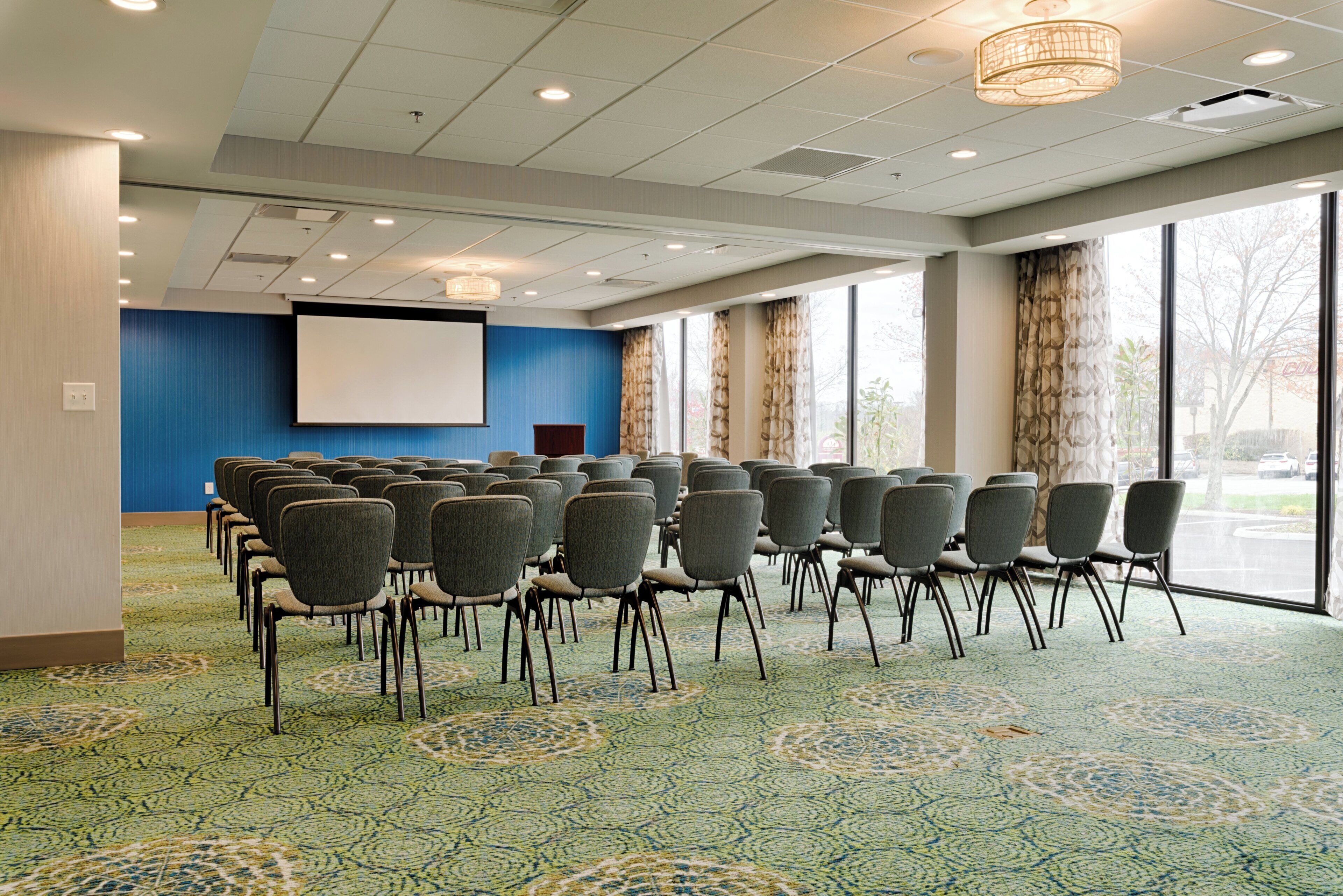 A conference room with rows of chairs, a projector screen, and large windows.
