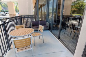 Un espacio al aire libre con una mesa redonda y sillas, un sofá y una barandilla de vidrio.