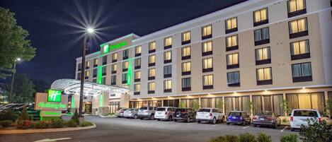 A Holiday Inn hotel with a modern facade, multiple floors, and a parking lot with several cars.
