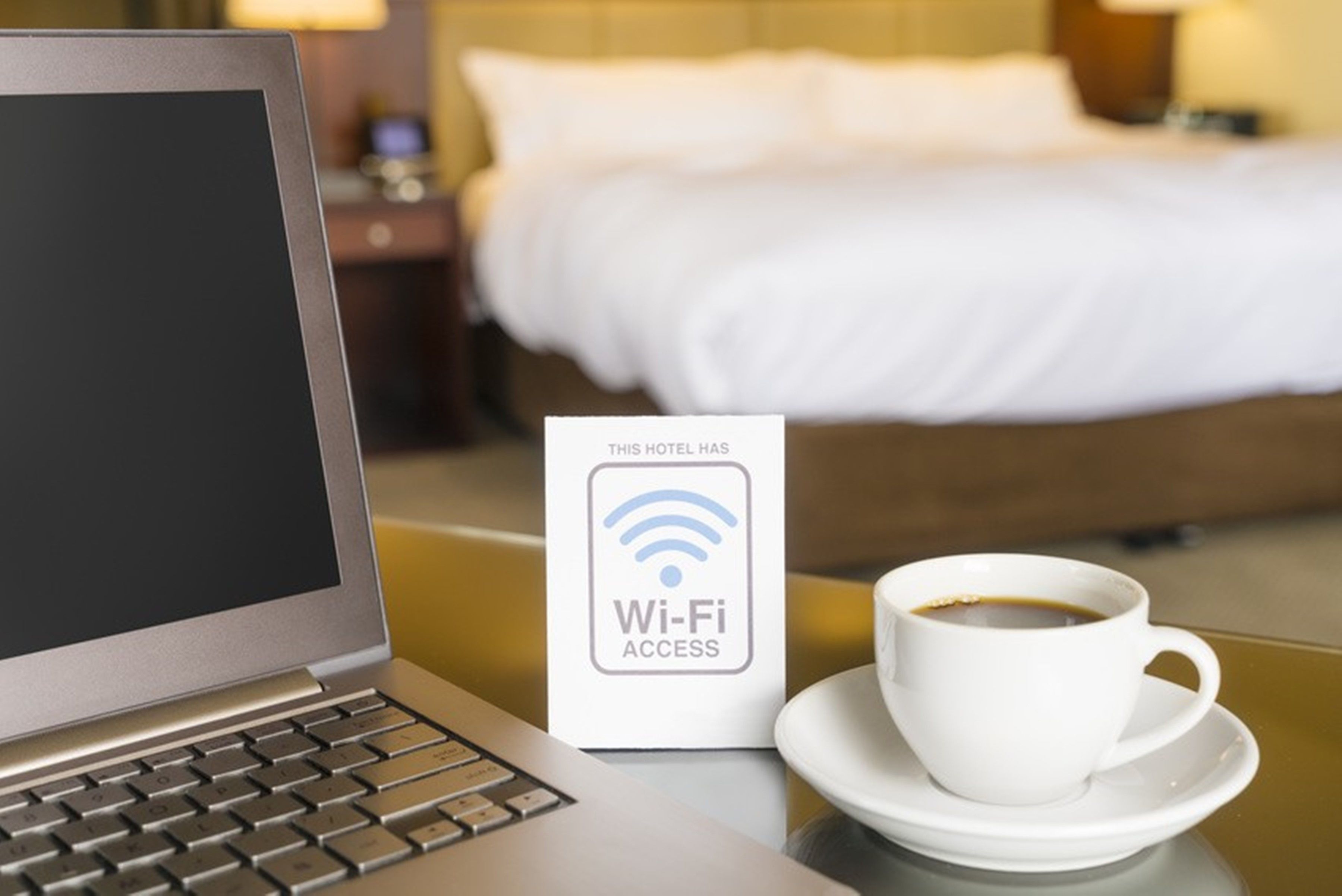 Een laptop, een Wi-Fi toegangssign en een kop koffie op een hoteltafel.