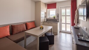 A modern kitchenette with a dining area, a sofa with orange cushions, and a small table with a fruit bowl. - TRIO Apartment Hotel Berlin (Berlin)