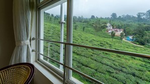 Una habitación con un amplio ventanal que da a una exuberante plantación de té verde y una casa distante.