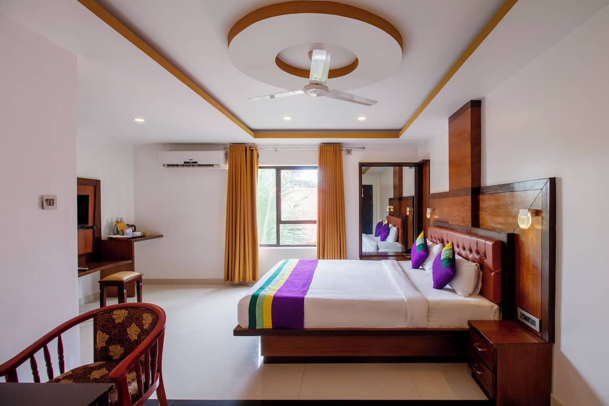 Habitación de hotel con cama, escritorio, silla, ventilador de techo y ventana con cortinas.