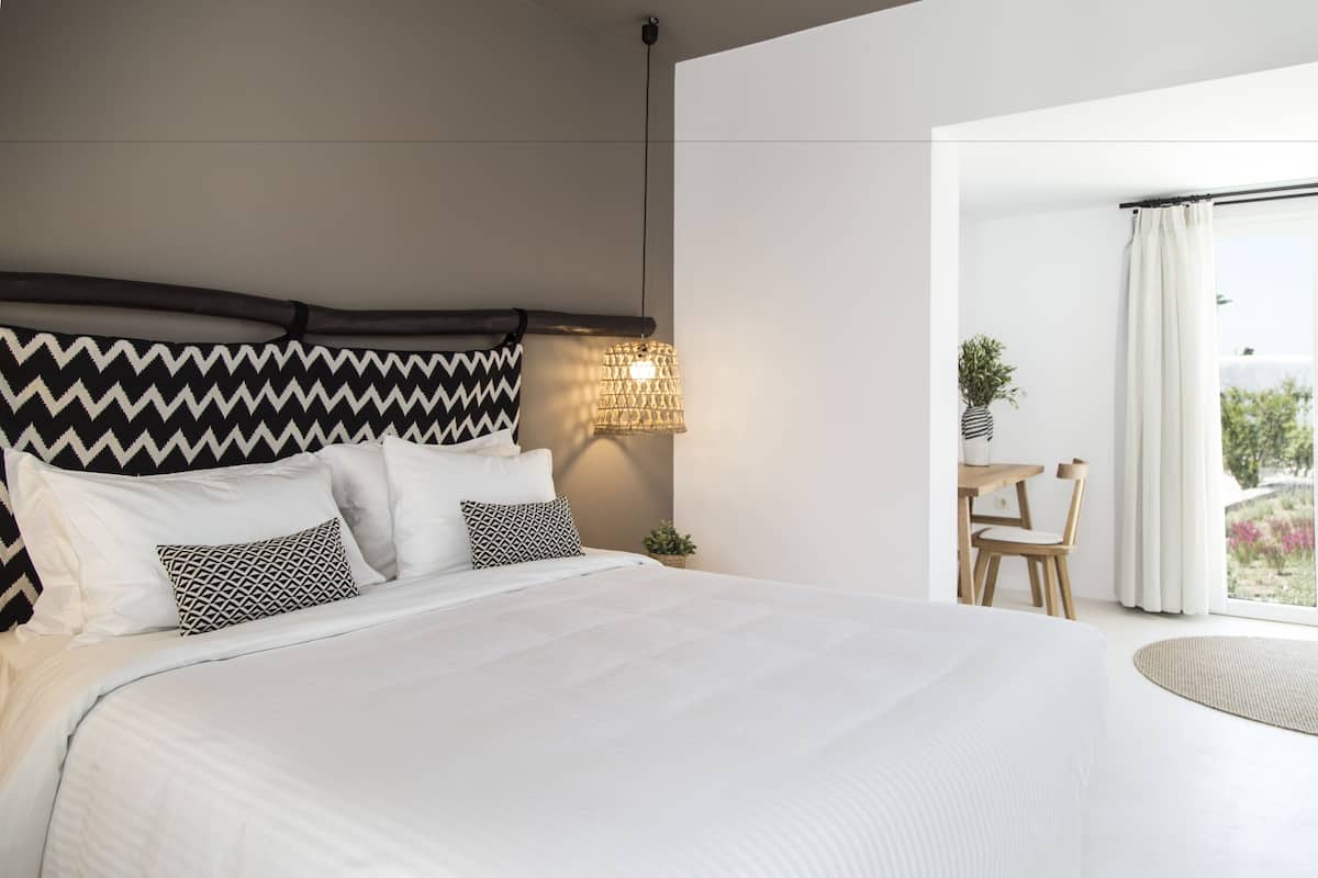 Une chambre à coucher moderne avec un grand lit, une table de chevet, une lampe et une vue sur l’extérieur.