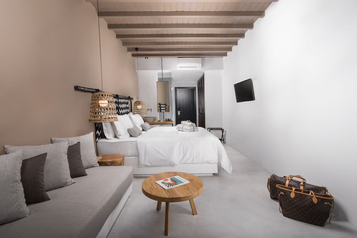 Une chambre d’hôtel moderne équipée d’un lit, d’un canapé, d’une table de chevet et de deux sacs à main.
