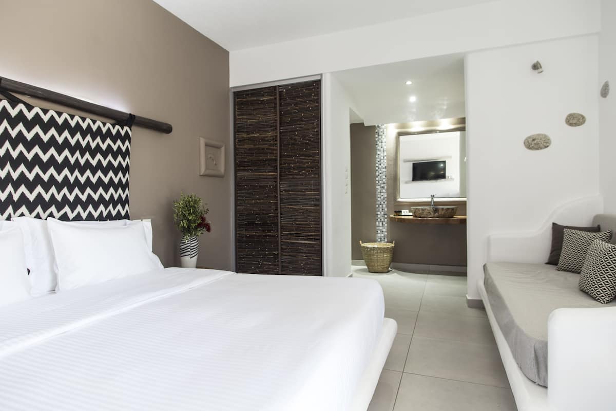 Une chambre d’hôtel moderne dotée d’un grand lit, d’un canapé, d’une salle de bain avec un miroir et d’un petit coin cuisine.