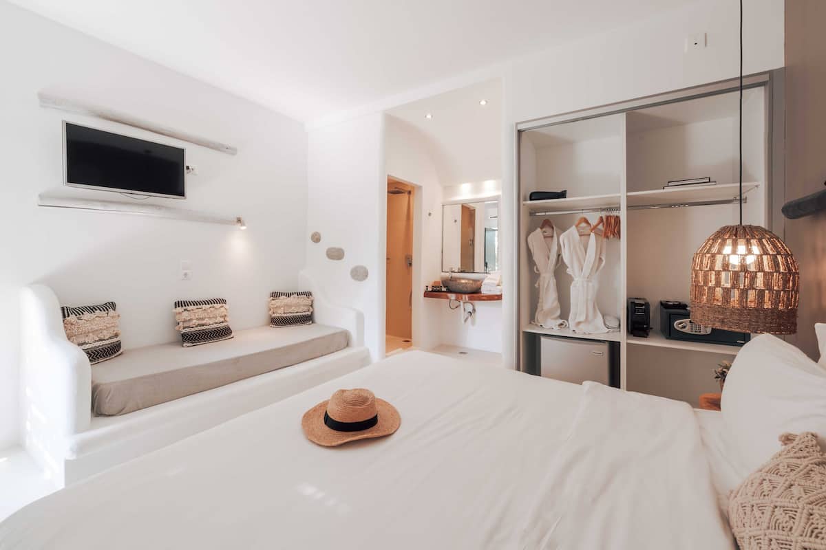 Une chambre d’hôtel moderne dotée d’un grand lit, d’un téléviseur fixé au mur, d’une armoire et d’un coin salon avec des coussins.