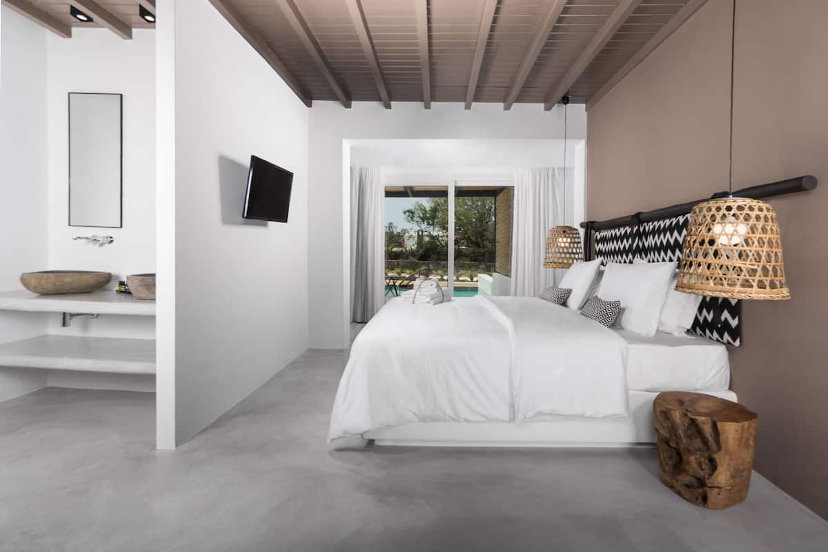 Une chambre moderne avec un grand lit, une télévision, une table de chevet en bois et une vue sur l’extérieur.