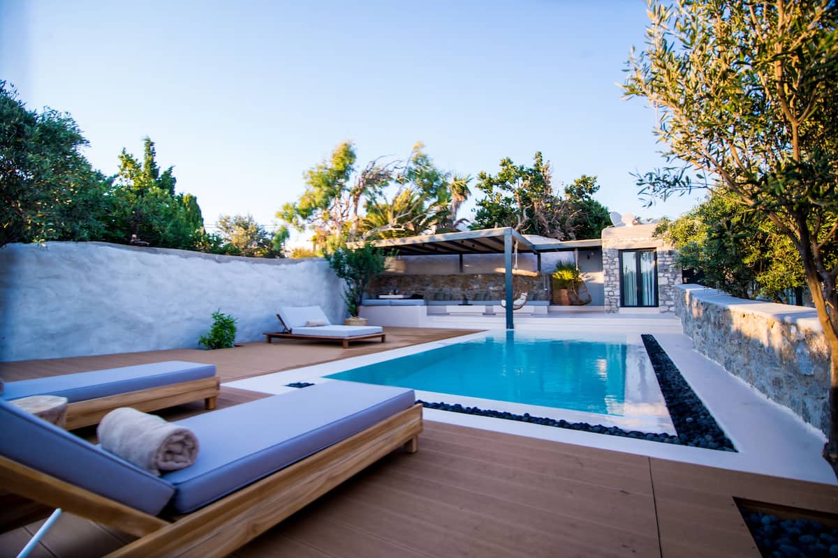 Un espace piscine extérieur moderne, doté de chaises longues, d’une pergola et d’un mur en pierre.