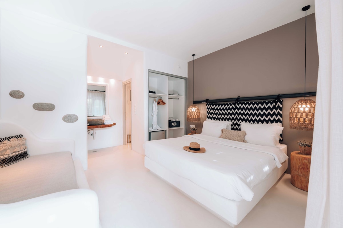 A modern bedroom with a large bed, a wardrobe, a vanity, and a seating area.