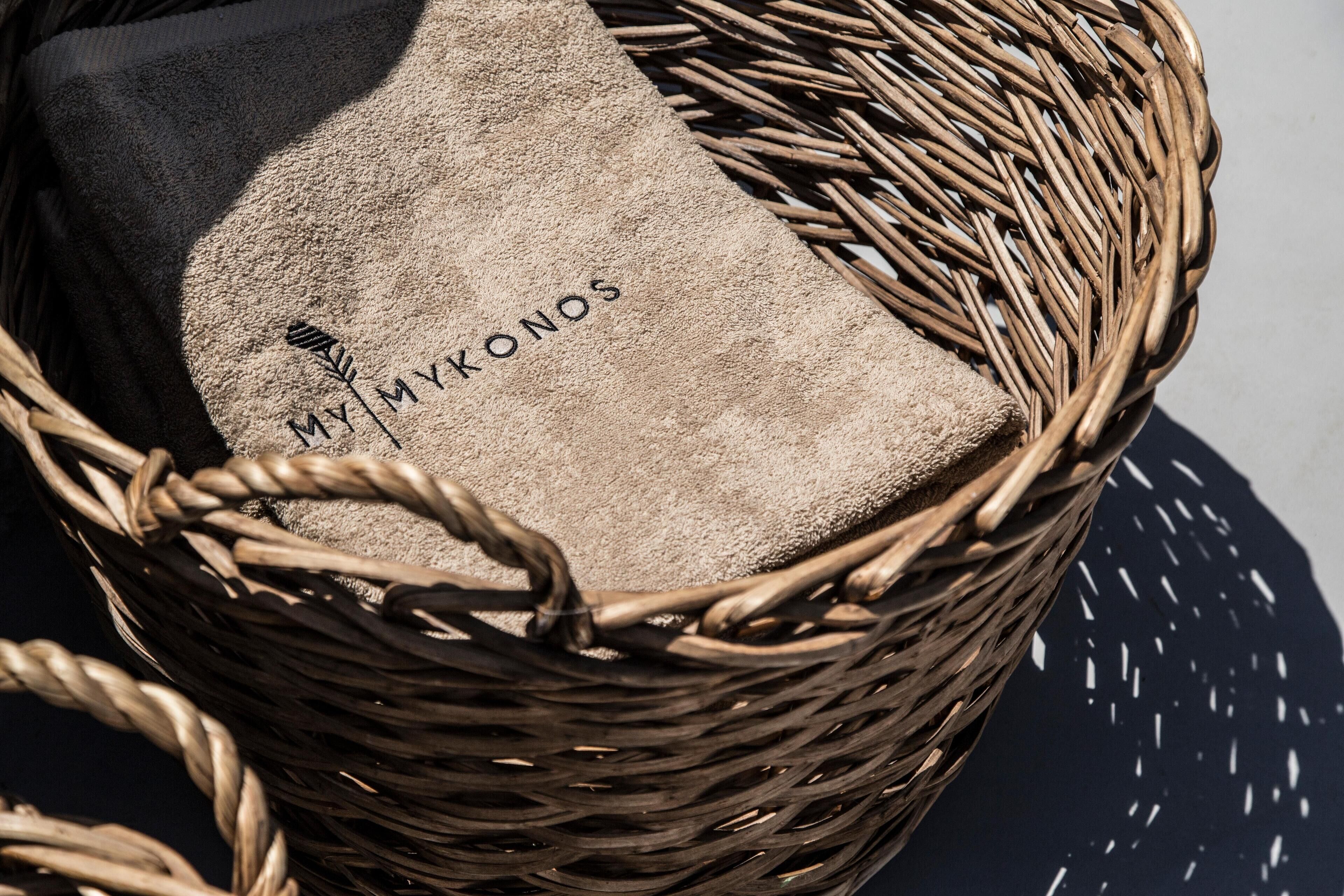 Una cesta de mimbre con un cojín color beige, con la etiqueta 'MY MYKONOS'.