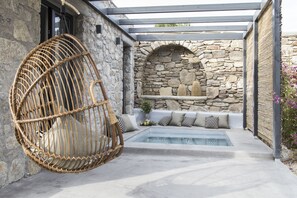 A stone-walled outdoor area with a hot tub, a hanging wicker chair, and a built-in seating area with cushions. - My Mykonos Boutique by Mr and Mrs White (Mykonos)