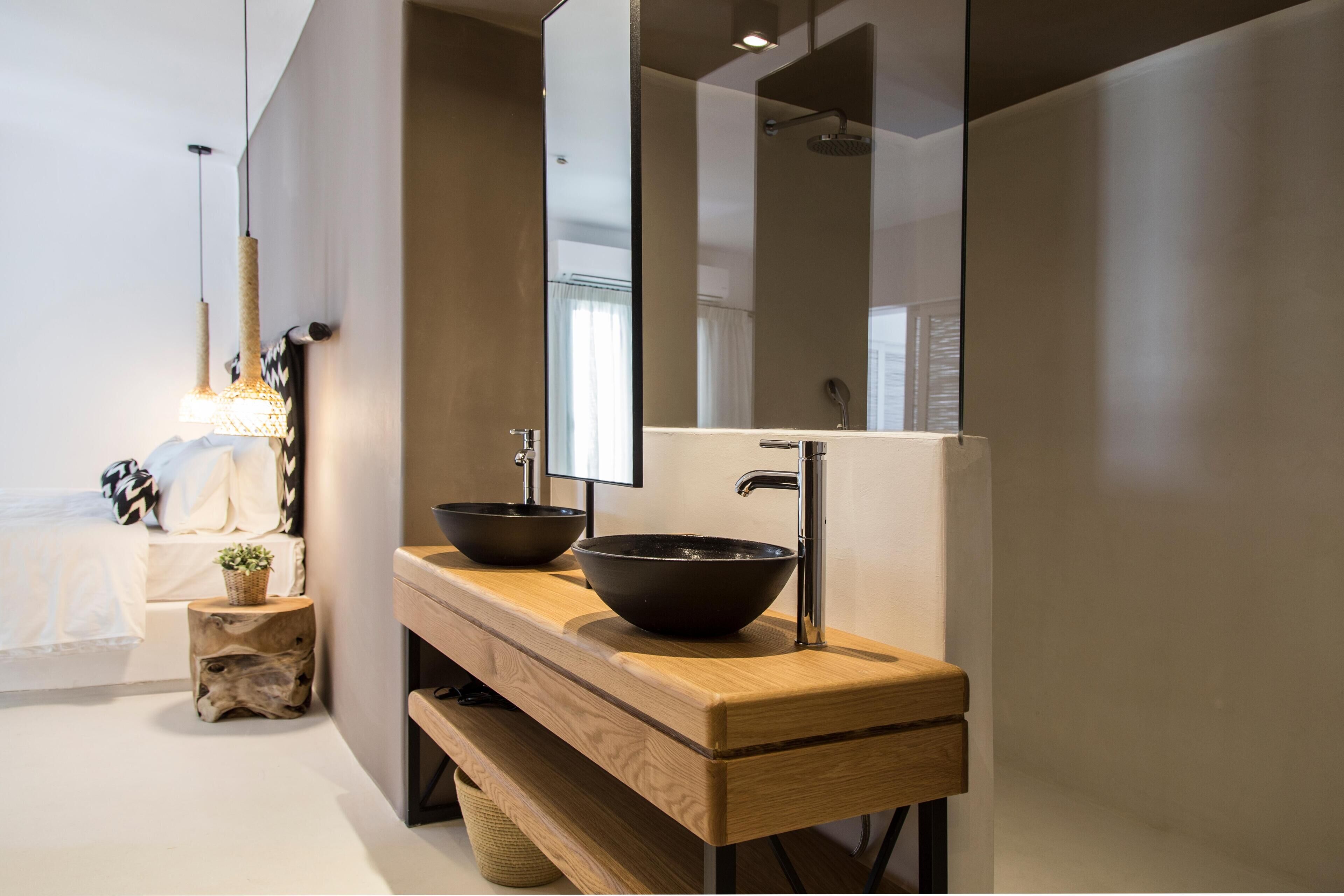 A modern bathroom with a wooden vanity, two black vessel sinks, a large mirror, and a hanging light fixture.