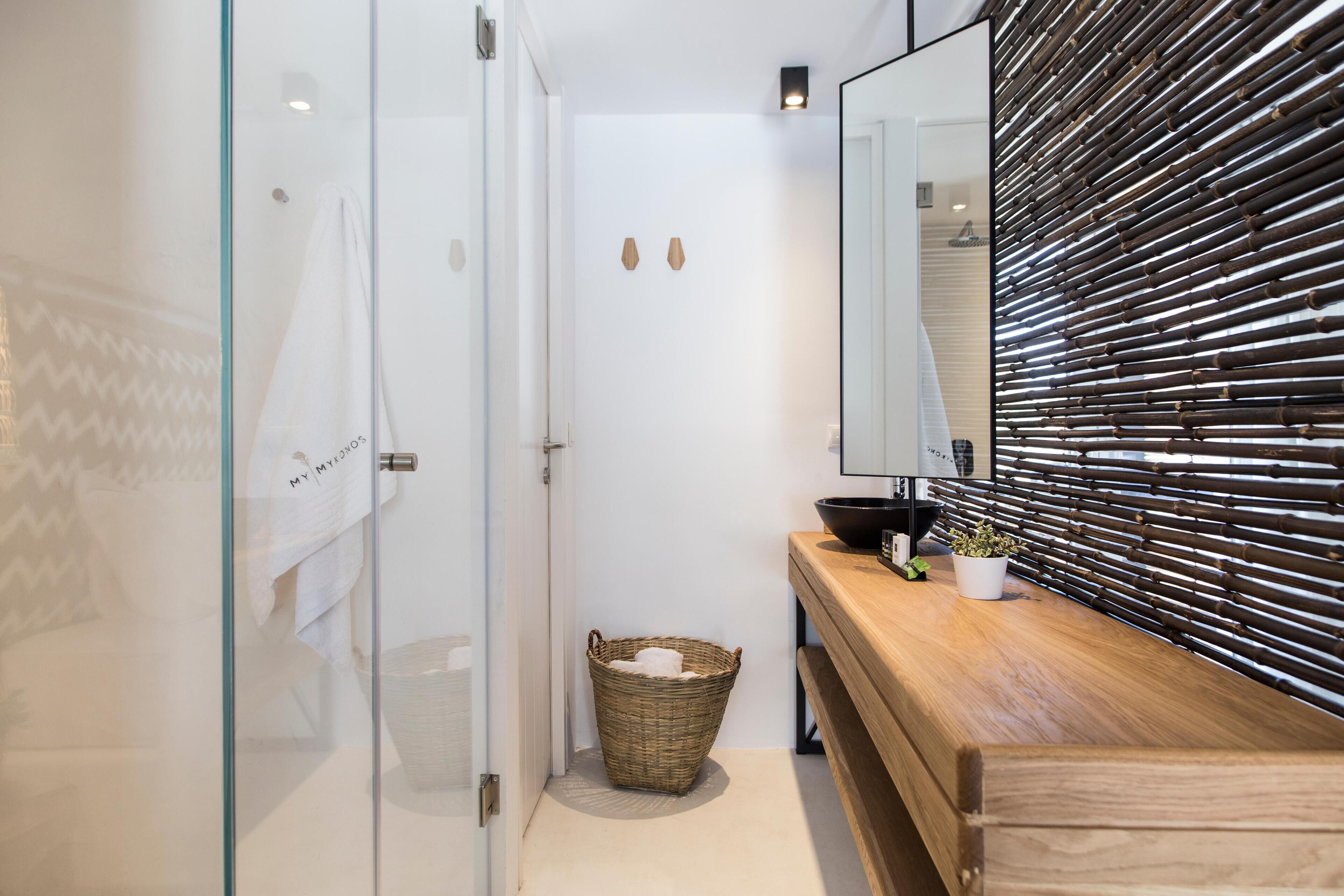 Un baño moderno con cabina de ducha de vidrio, tocador de madera y panel de pared de bambú.
