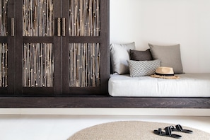 A modern living room with a dark wooden wall panel, a light grey sofa with patterned cushions, and a woven rug. - My Mykonos Hotel by Mr and Mrs White (Mykonos)