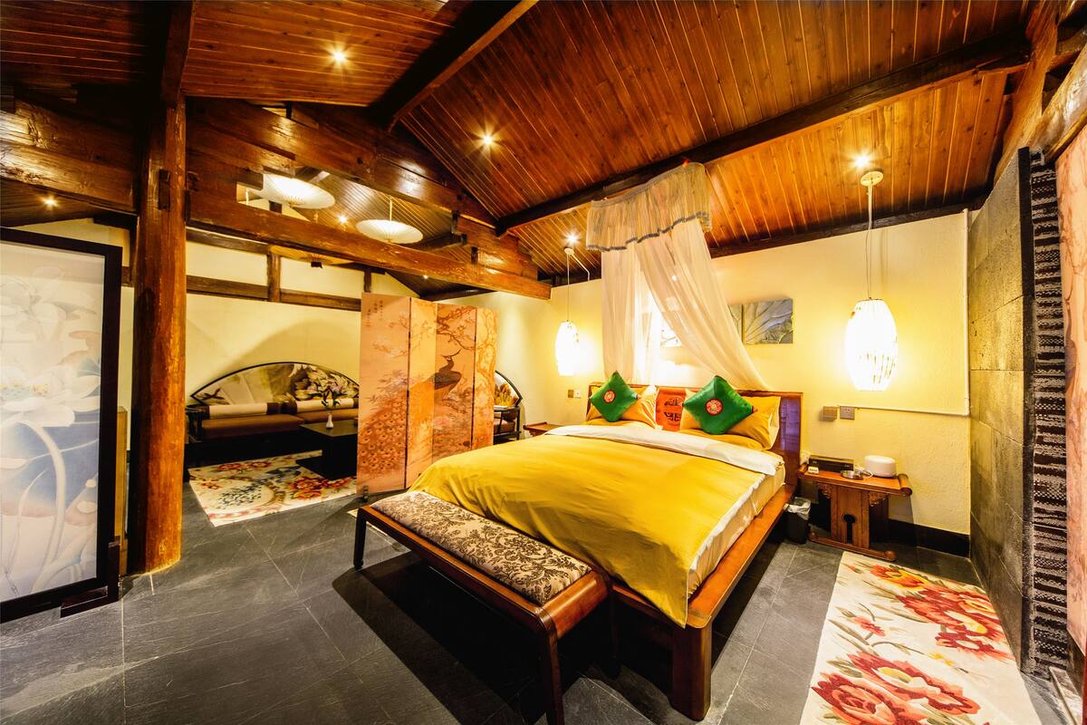 A spacious bedroom with a large bed, a bench, and a wooden ceiling.