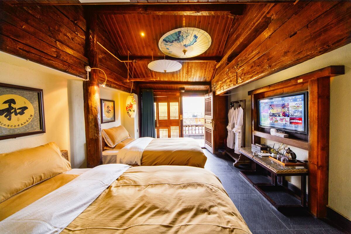 A traditional Japanese-style room with wooden beams, two beds with beige bedding, a television, and a sliding door leading to a balcony.