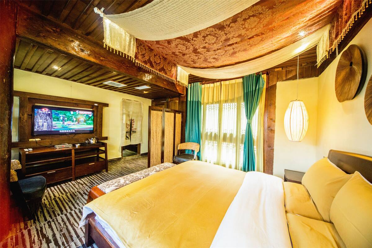 A spacious room with a large bed, a television, and a wooden ceiling.